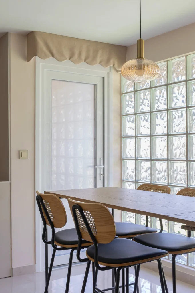 Comedor junto a la cocina con mesa de madera, sillas oscuras y pared de vidrio translúcido.