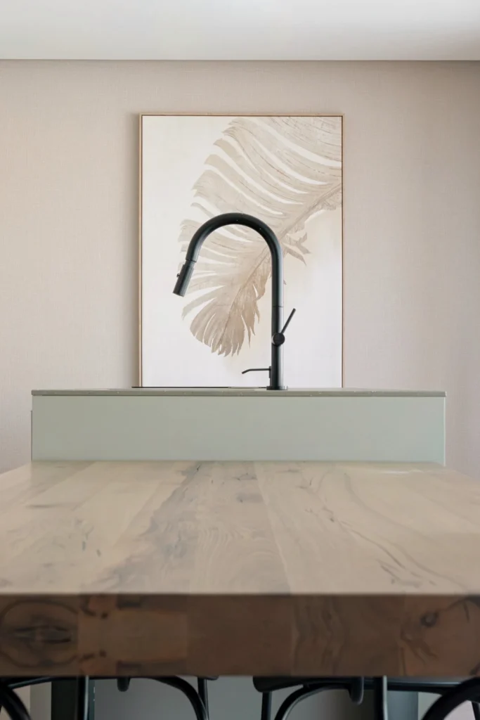 Detalle de la grifería negra frente a la mesa de madera y un cuadro en tonos neutros.